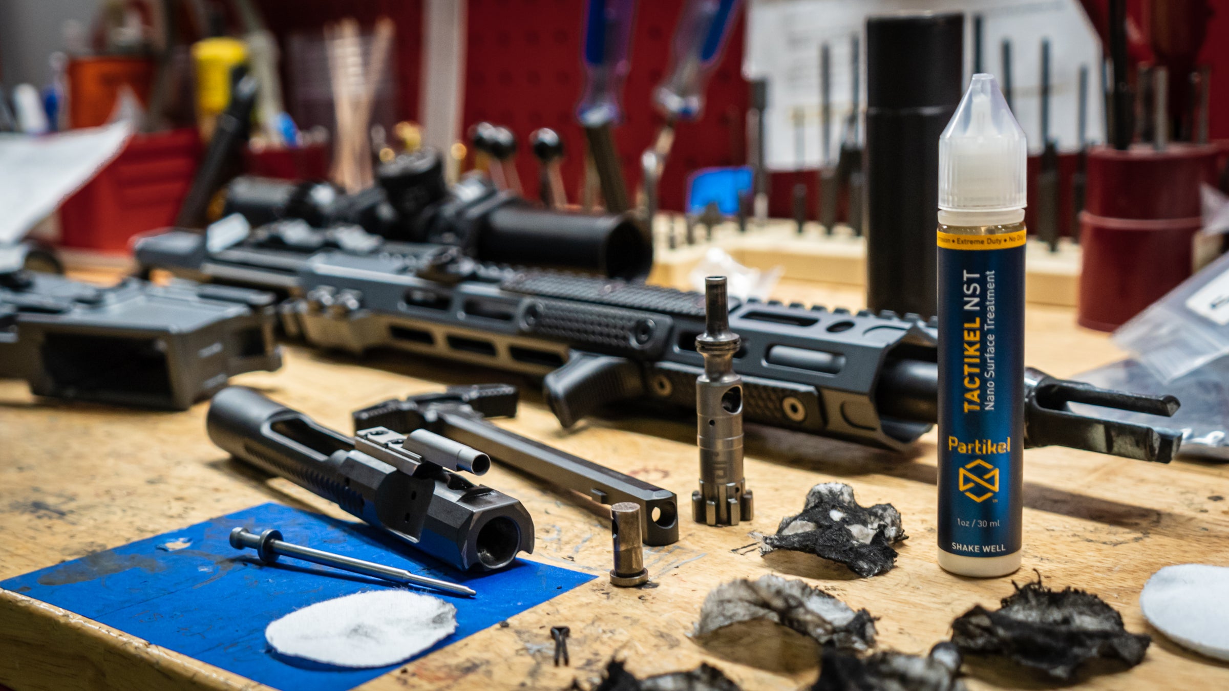 Gunsmith's workbench with disassembled TX-15 rifle. Shows Bolt Carrier Group after cleaning. A bottle of Tactikel NST is in the foreground.